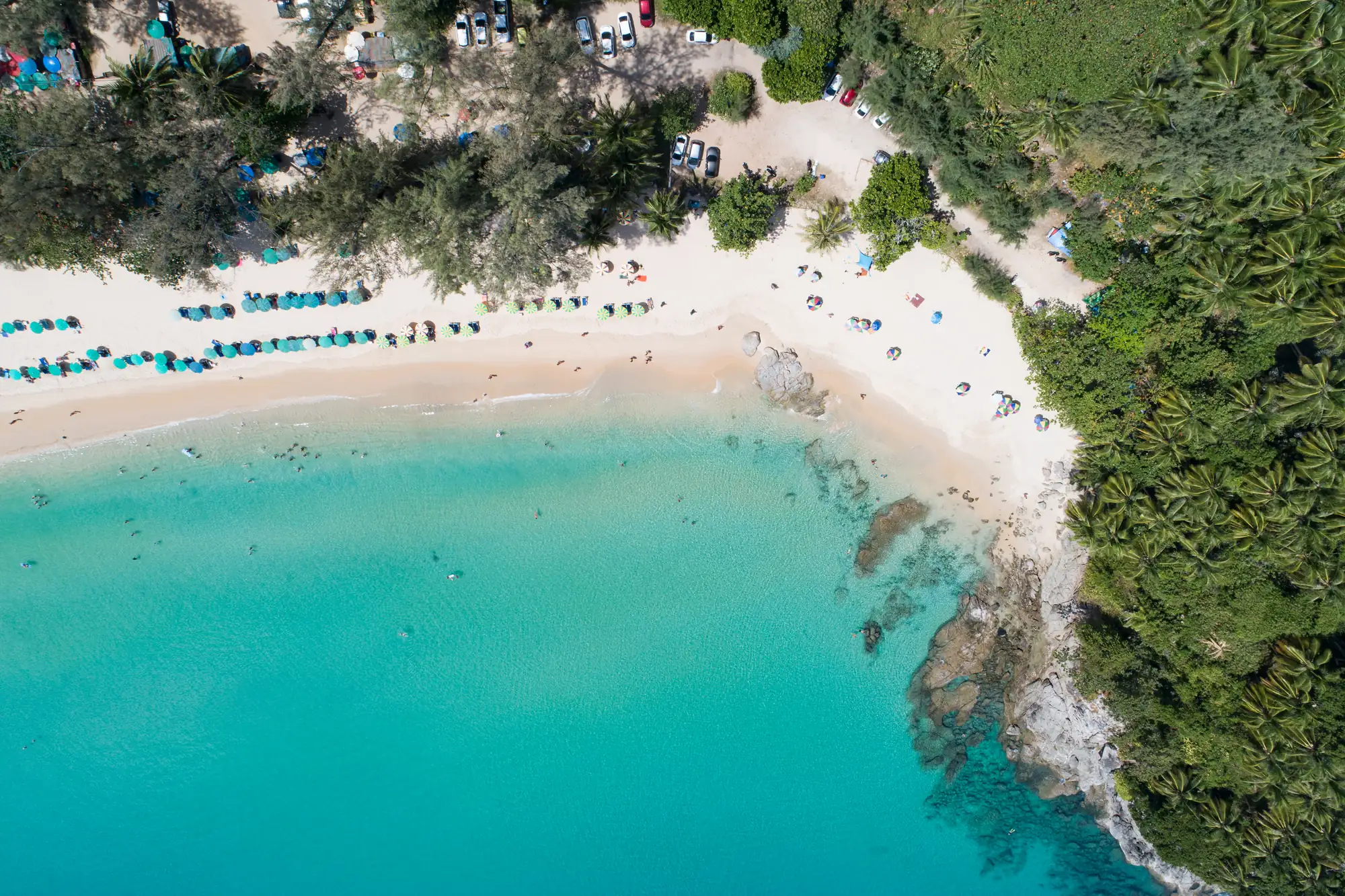 Aerial view of Bang Tao beach: white sand, sun loungers and the sea along a wooded shore