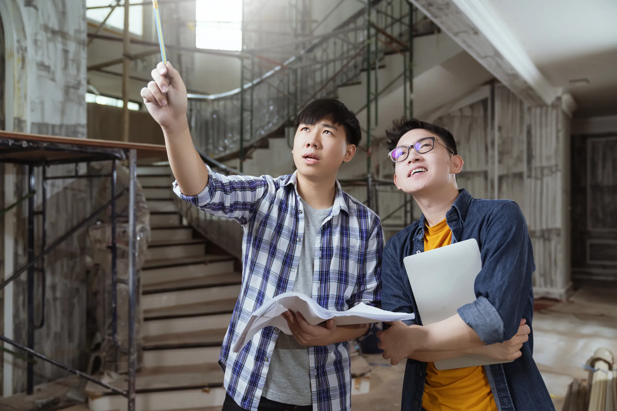 A contractor and a designer holding drawings point at work in progress inside an unfinished house