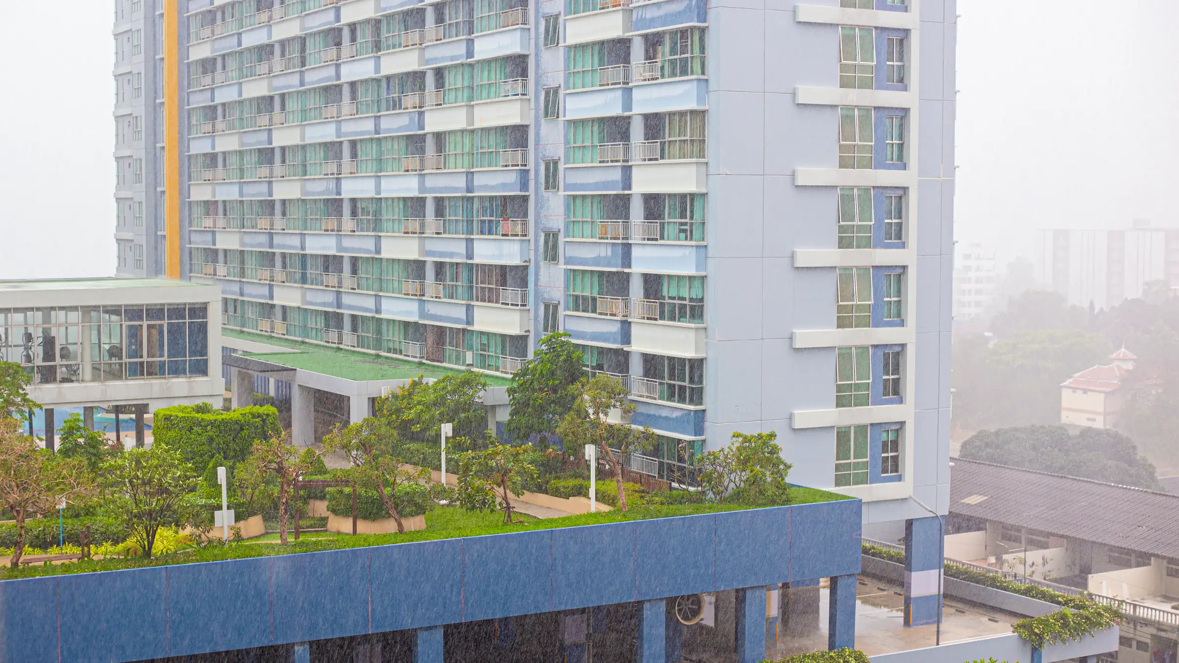 High-rise condominium building overlooking a landscaped pool deck on a rainy day in Thailand