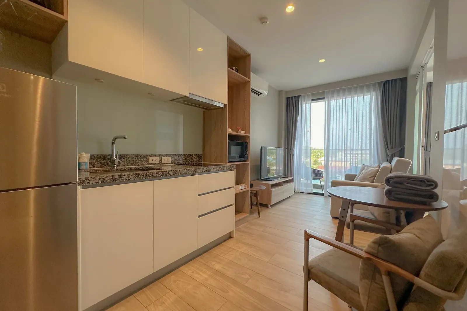 Open-plan kitchen and living room of a furnished 1-bedroom condo with a balcony door