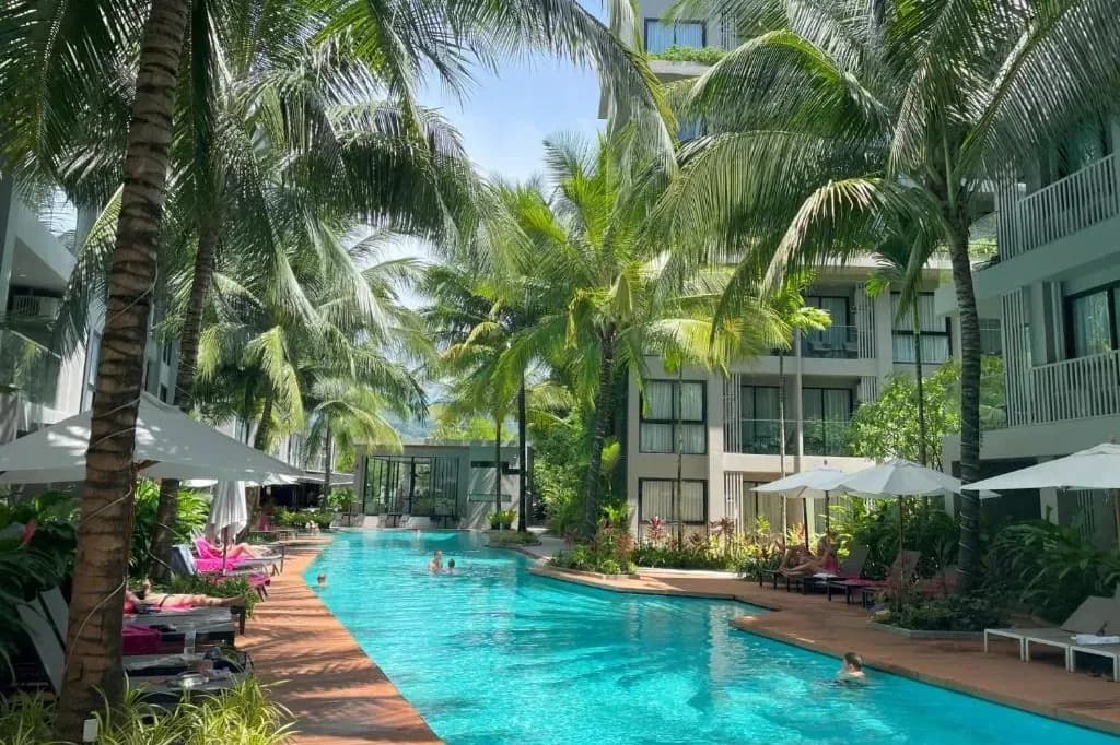 A long lagoon-style swimming pool lined with palm trees between low-rise condominium buildings