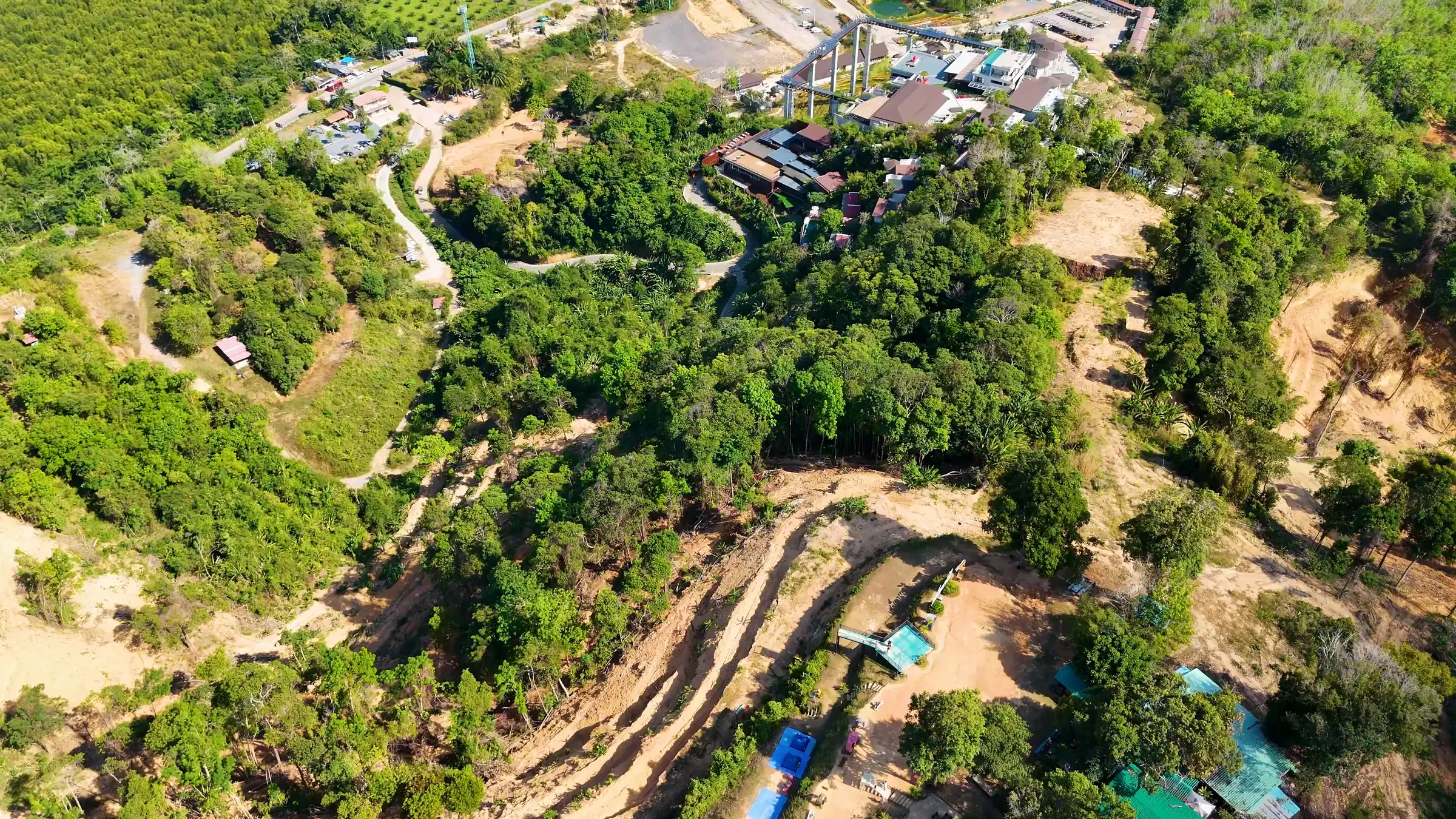 Aerial view of a green hillside cut by new access roads and cleared building plots, with plantations behind