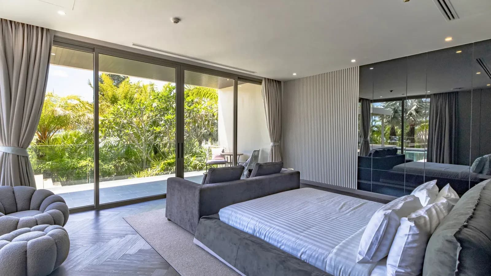 A villa bedroom with floor-to-ceiling glass doors opening onto a tropical garden