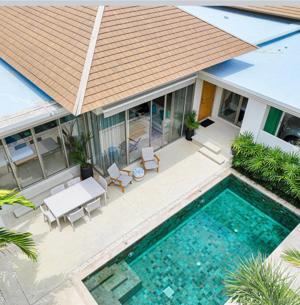Aerial view of a modern three‑bedroom pool villa with emerald‑tile swimming pool, outdoor dining set, and lounge chairs in Laguna Phuket, offered for long‑term rental.